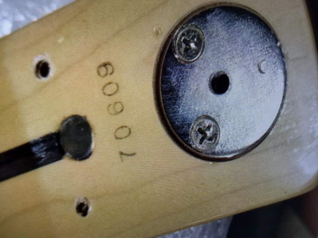 Close-up view of a wooden surface with circular metal plate, visible screws, and the number '70609' engraved.