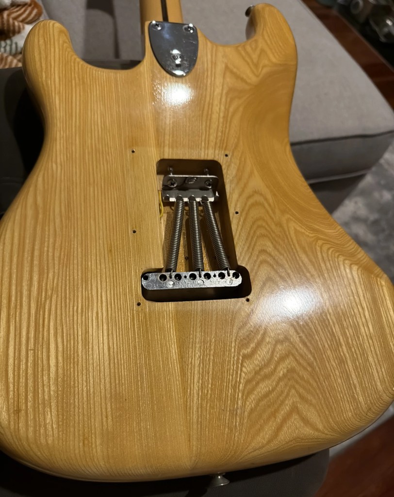 Close-up view of the back of an electric guitar showing its natural wood grain finish and bridge assembly.